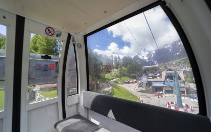 Interior of a cable car with no-smoking sign, gray benches, and views of trees, a road, and mountains.