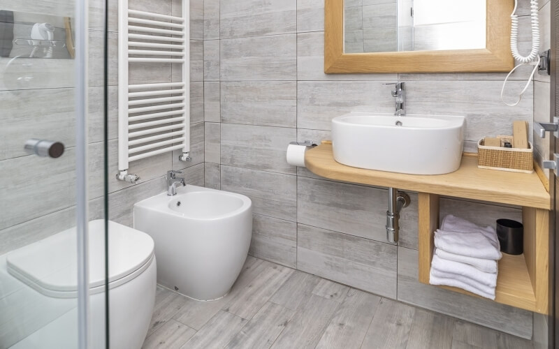Bagno moderno con piastrelle in pietra, lavabo in legno chiaro, doccia, bidet e decorazioni minimaliste.