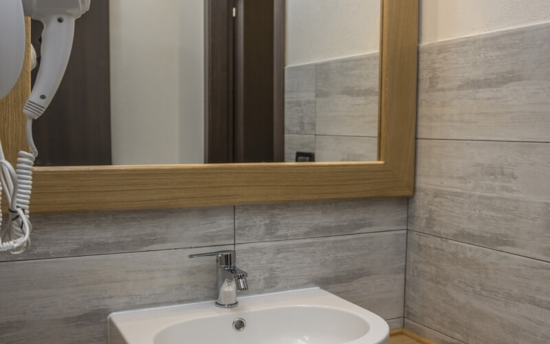 A clean bathroom with a white sink, large mirror, wall-mounted hair dryer, and elegant gray tiled walls.