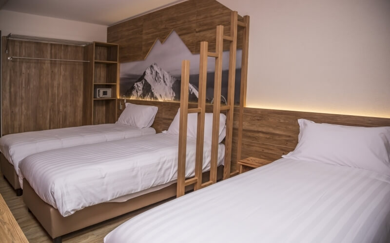 Cozy hotel room with two wooden beds, a ladder, a closet, and a black-and-white mountain picture above the beds.