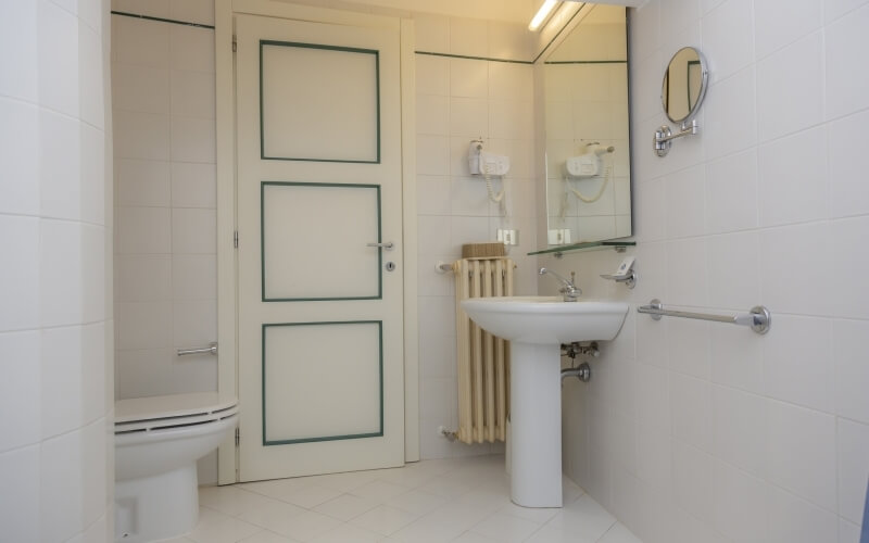 A clean, white bathroom featuring a toilet, sink, shower, and green trim accents, with modern fixtures and tiled walls.