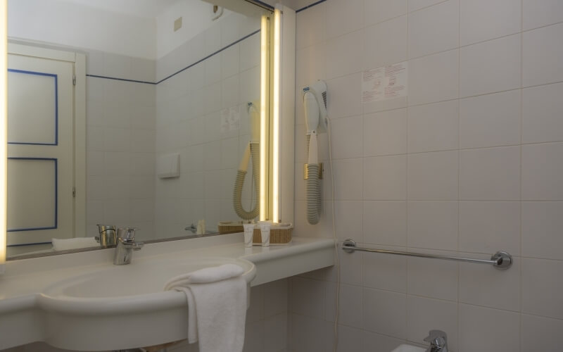 Bagno pulito con specchio grande, lavabo centrale, asciugamano bianco e accessori pratici, tutto in un'atmosfera accogliente.