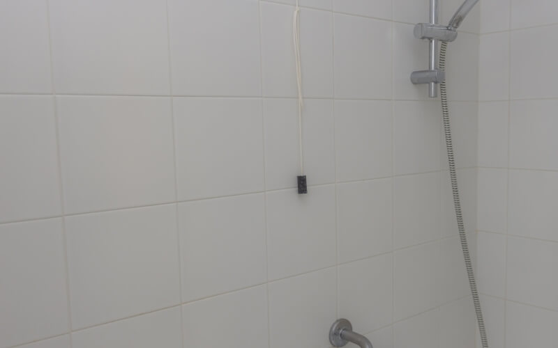 Modern shower area with white tiles, silver shower head, black sensor, and silver control knob. Clean and sleek design.