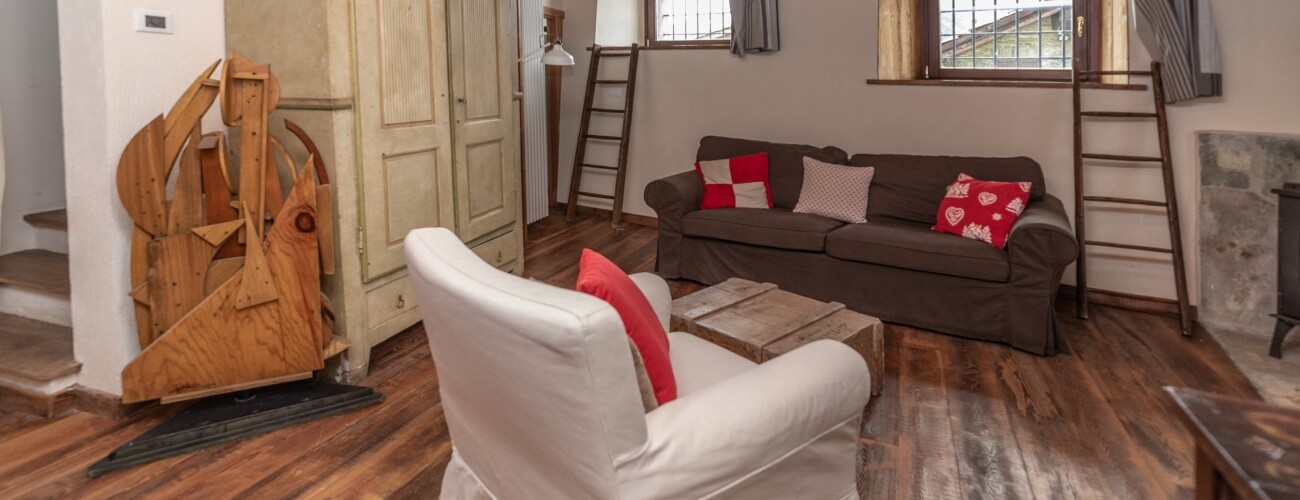 Cozy living room with a brown couch, white armchair, wooden coffee table, rustic staircase, and white cabinet.