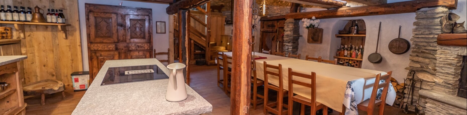 Rustic country kitchen and dining area with wooden accents, a white island, and a cozy table setting under a wooden beam.