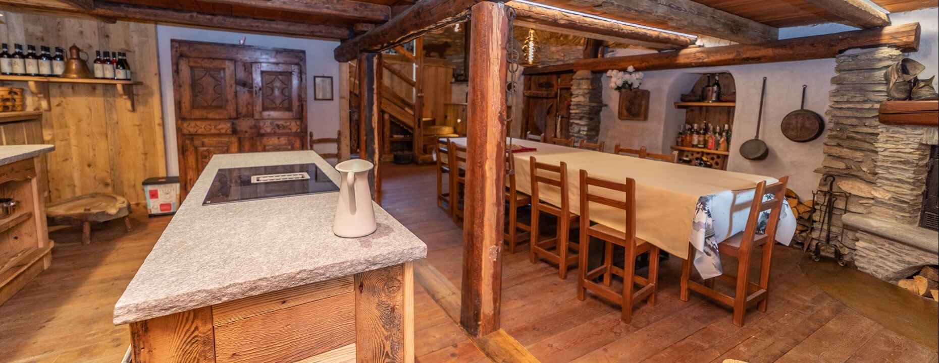 Rustic kitchen and dining area with wood and stone, featuring a granite island, fireplace, and cozy decor.