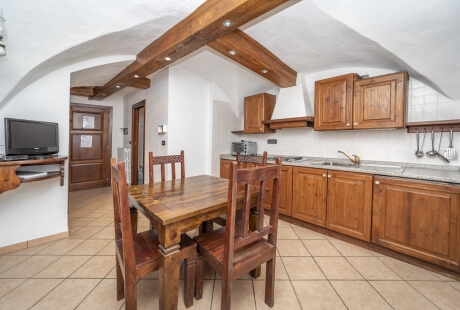 Cozy kitchen with arched ceiling, wooden cabinets, dining area, and light brown tile flooring.