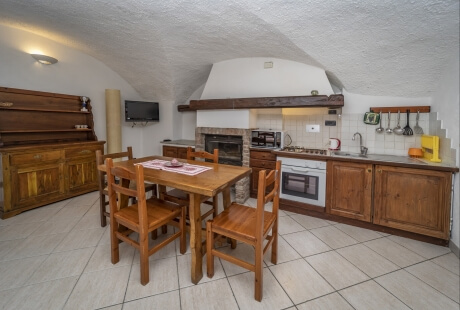Rustic dining and kitchen area featuring tiled floors, wooden table, modern appliances, and a slanted white ceiling.