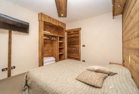 Cozy guest room with rustic and modern elements, featuring a bed, wooden accents, and a mounted TV.
