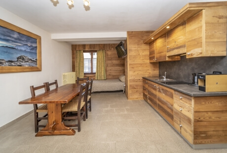 A kitchen and dining area with light wood cabinets, a dining table, and a window with yellow curtains in an open-plan space.