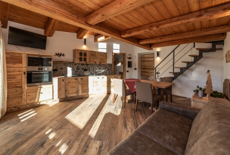 Modern open-plan living space with kitchen, dining area, wooden beams, staircase, and natural light creating a cozy atmosphere.