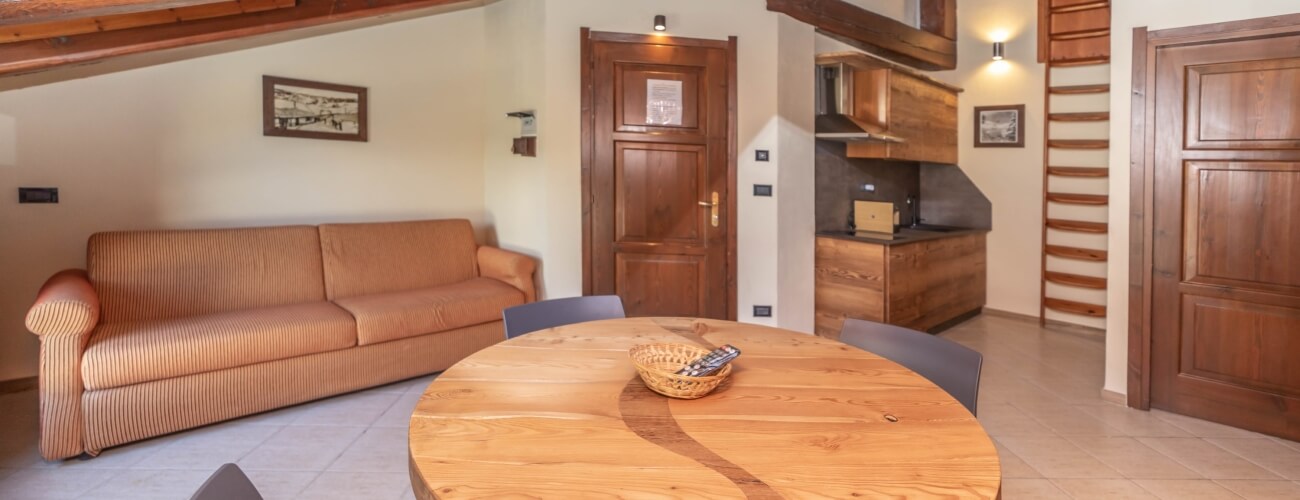 Cozy living room with an orange striped couch, dark chairs, wooden table, and a small kitchen with loft above.