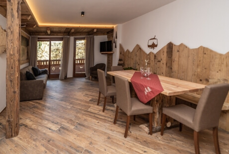 Cozy rustic dining and living area with wooden table, brown couch, and natural light from a window.
