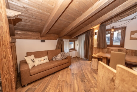Cozy living room with rustic wooden beams, leather couch, dining area, and natural light from a large window.