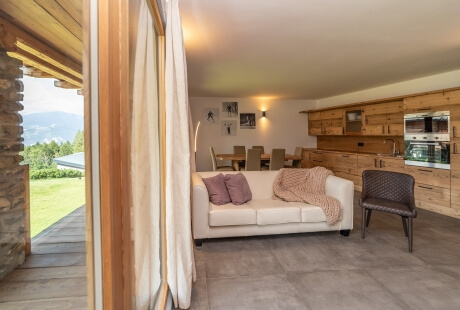 Area living minimalista con divano bianco, cucina in legno, sedia nera e vista montagna illuminata.