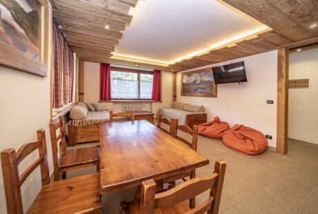 Una stanza luminosa con un tavolo da pranzo, divano, due pouf, decorazioni murali e soffitto in legno con travi a vista.