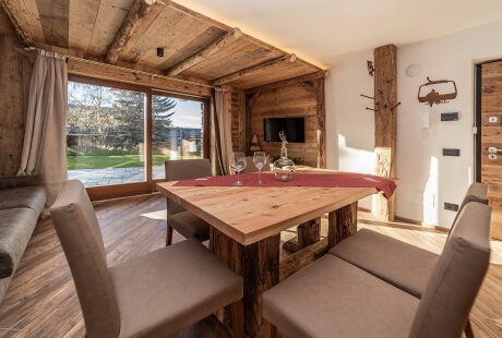 Cozy dining room with a wooden table, beige chairs, a couch, and large windows showcasing a serene outdoor view.