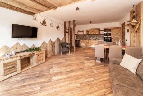 Rustic living area and kitchen with wood beams, flat-screen TV, dining table, and metal moose decor.