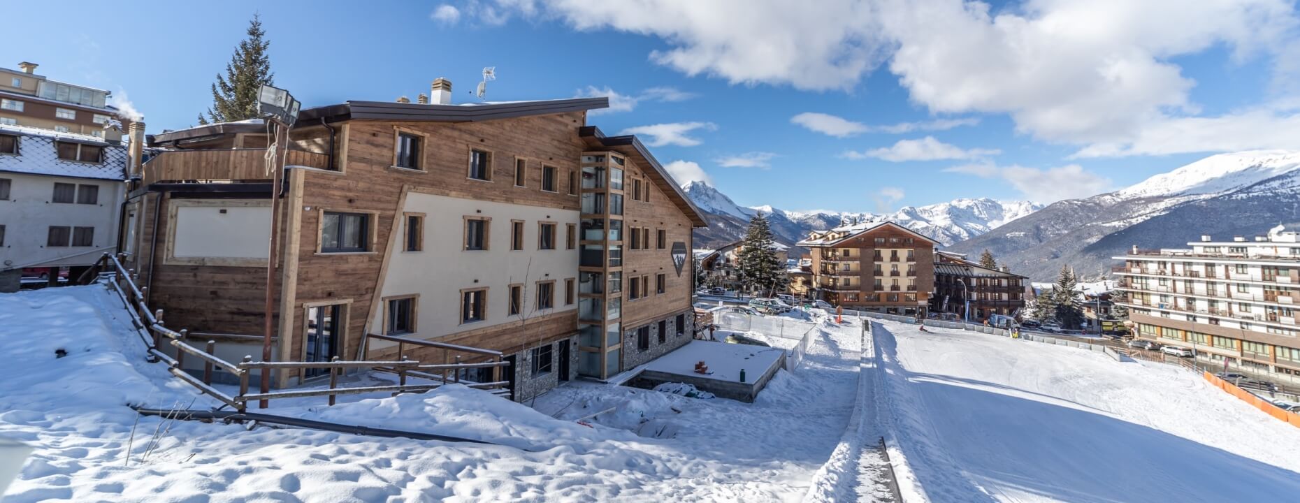 Snow-covered scene with a wooden and stone building, mountains in the background, and a "Hotel" sign visible.