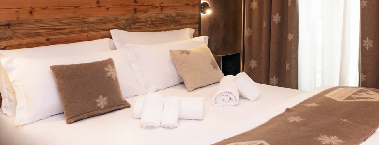 Cozy hotel room featuring a bed with white pillows and a brown snowflake-patterned blanket, minimalist decor, and a lamp.