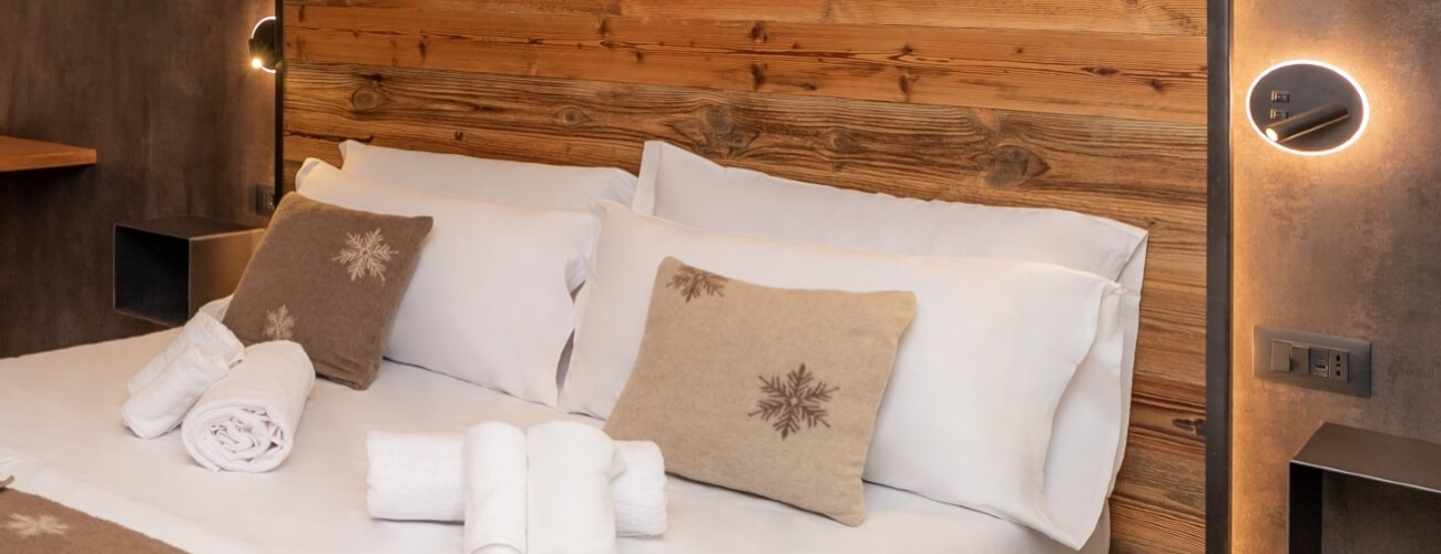 Cozy hotel room with a bed, white linens, snowflake pillows, wooden headboard, and warm lighting for a relaxing atmosphere.