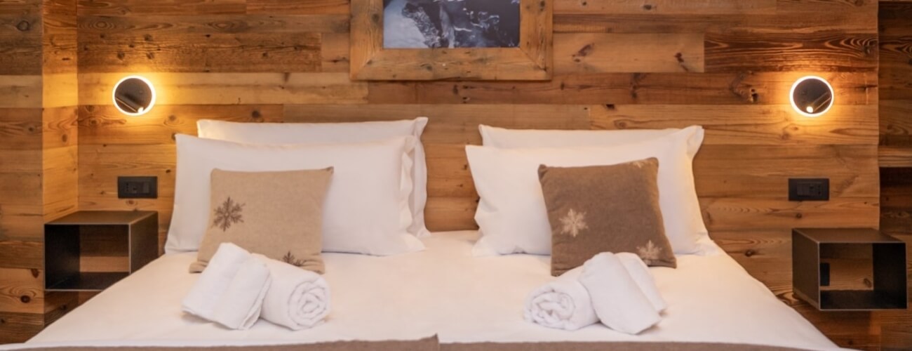 Camera da letto accogliente con un grande letto, cuscini decorati e pareti in legno chiaro, trasmette serenità e tranquillità.