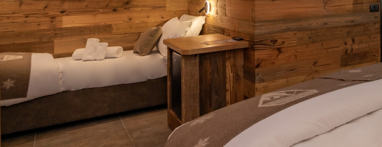 Camera d'hotel accogliente con due letti, pareti in legno e pavimento piastrellato, atmosfera serena e confortevole.