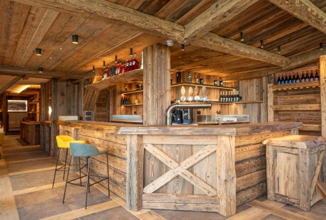 Cozy wooden bar with a countertop, two chairs, and rustic wooden walls and shelves in the background.