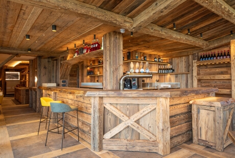 Interno di un bar rustico con sgabelli colorati, bar in legno, illuminazione calda e area cucina sullo sfondo.