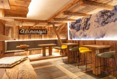 Ristorante rustico moderno con murale di montagne, tavoli in legno, booth grigi e soffitto a travi in legno.