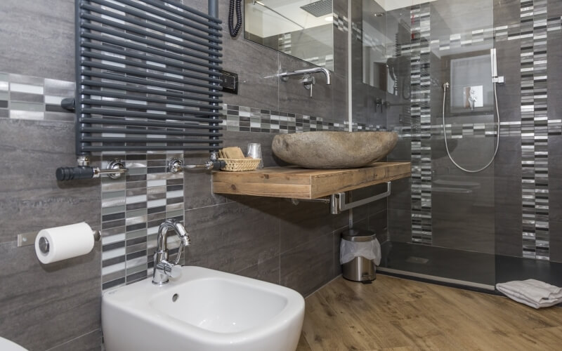 Modern bathroom with gray tiles, wooden sink platform, shower with glass door, toilet, and towel rack. Clean and contemporary design.