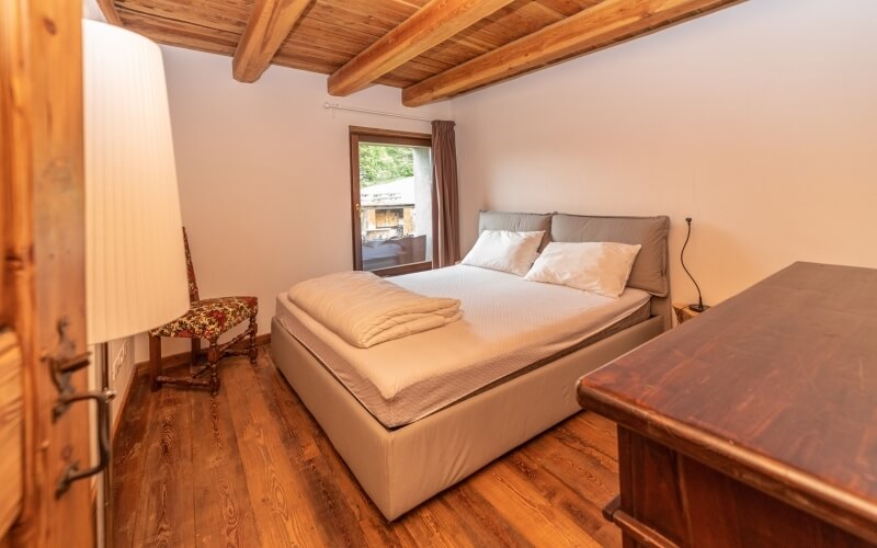 Serene bedroom with a spacious bed, warm lighting, wooden chair, and a view of lush greenery through the window.