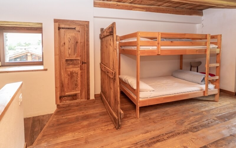 Cozy room with a bunk bed, wooden flooring, white walls, and a window, creating a simple rustic atmosphere.