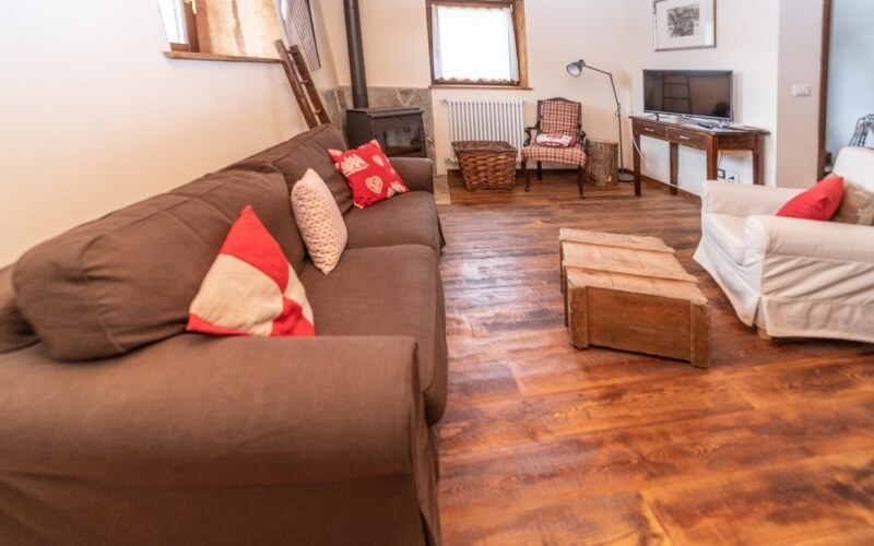 Cozy living room with a brown couch, red and white pillows, wooden fireplace, dark table, and warm wooden floor.
