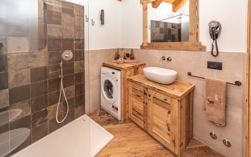 Rustic bathroom with a walk-in shower, wooden vanity, and washing machine, featuring earthy tones and cozy decor.