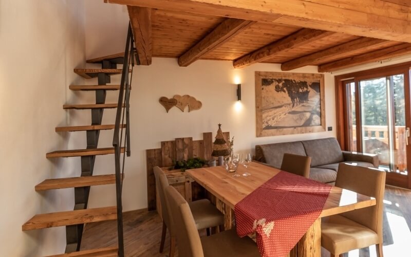 Cozy dining area with a wooden table, gray couch, landscape painting, spiral staircase, and a glass door to the outside.