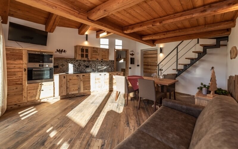 Un accogliente soggiorno e cucina con soffitto in legno, divano marrone, tavolino, albero di Natale e luce naturale.
