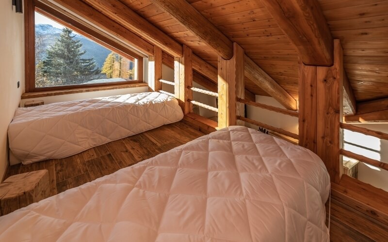 Cozy attic room with two beds, wooden floors, sloping ceiling, large window, and serene decor for a tranquil retreat.