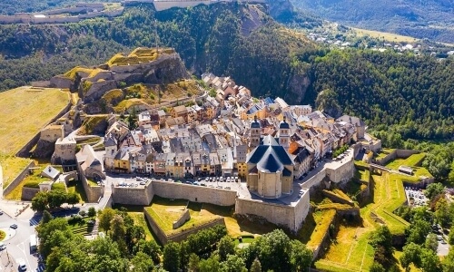 Castle complex on a mountain with arched gateways, colorful rooftops, and a church, set in a rural Swiss landscape.