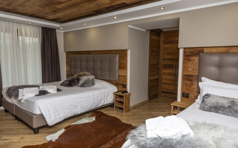 Cozy hotel room with two beds, tan and leather headboards, wooden table, cowhide rug, beige walls, and wooden ceiling.