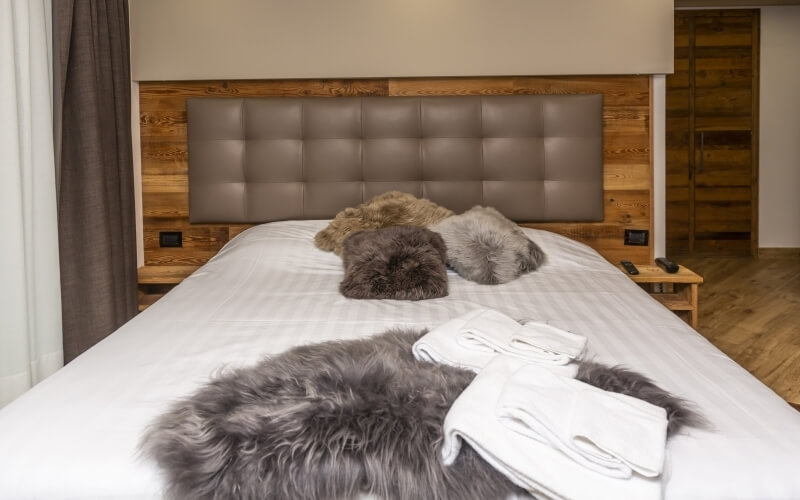 Cozy bedroom featuring a large bed with a leather headboard, furry pillows, and a wooden nightstand beside it.