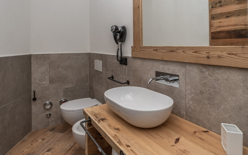 Rustic bathroom featuring a white sink, toilet, wooden accents, and a large mirror, creating a cozy, natural ambiance.