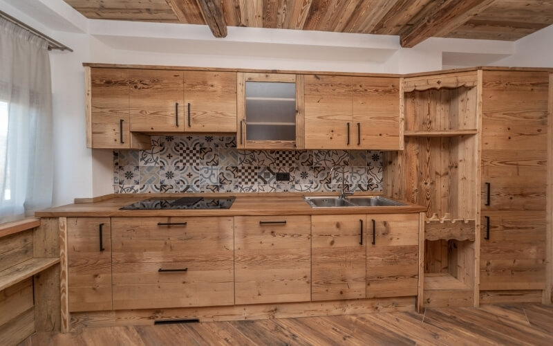 Modern kitchen with wooden cabinets, unique tile backsplash, stainless steel sink, and gas stove, exuding warmth and coziness.