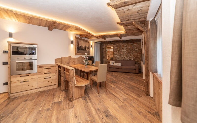 Modern rustic kitchen and living room with light wood floors, stainless steel appliances, wooden table, and cozy atmosphere.