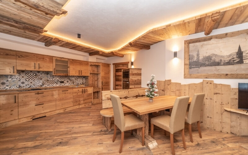 Spacious rustic room with wooden kitchen cabinets, a dining table, tan chairs, a Christmas tree, and warm lighting.
