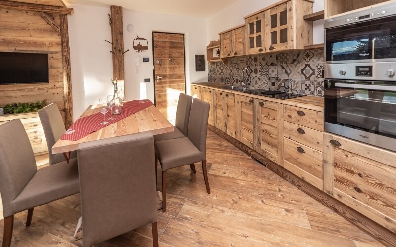 Cucina moderna con armadi in legno, forno in acciaio, tavolo da pranzo in legno e decorazioni floreali.