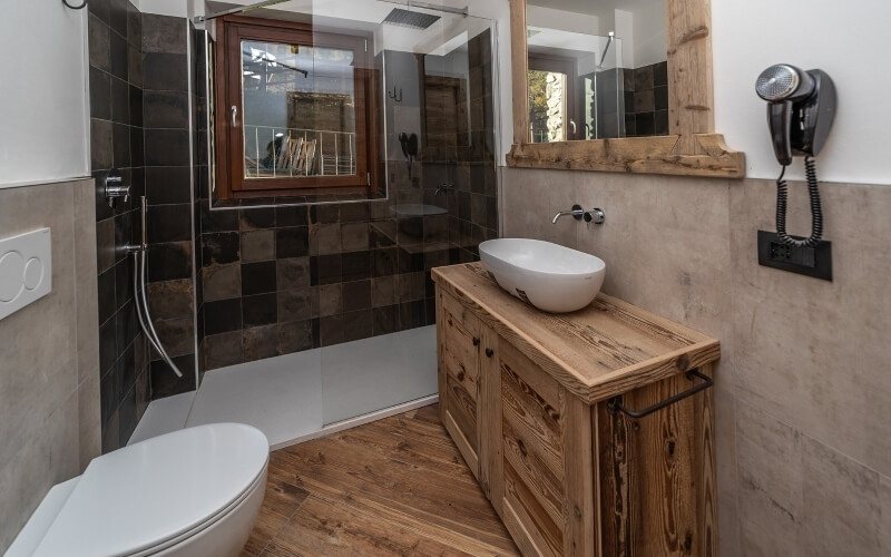 Bagno moderno con wc, lavabo in ceramica, doccia con piastrelle grigie e asciugacapelli nero montato a parete.