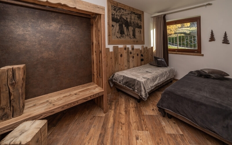 Camera rustica con due letti, panchina in legno, finestra con vista su alberi e decorazioni in legno.