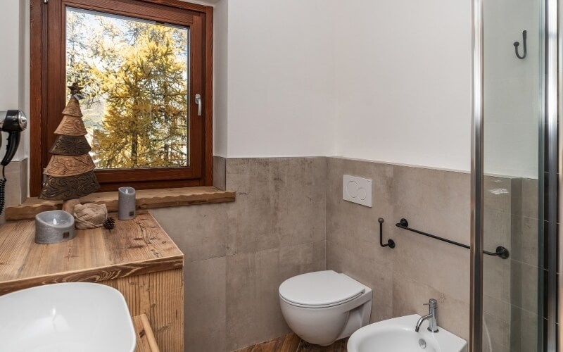 Rustic bathroom featuring a white toilet, oval sink, glass shower, and wooden accents, with a Christmas tree on the windowsill.