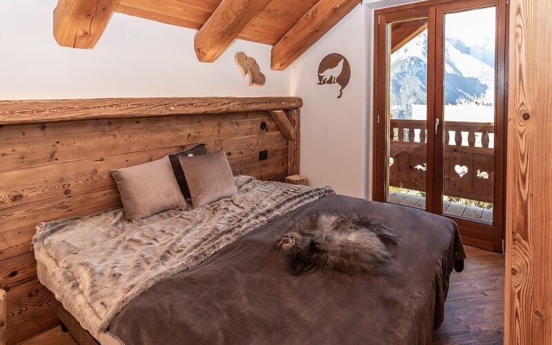 Cozy bedroom with a large bed, animal silhouettes on the wall, wooden beams, and a view of snow-covered mountains.